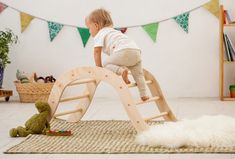 a toddler playing on a wooden swing set in a play room with toys and bunting