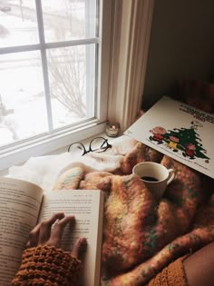 a person laying in bed reading a book and holding a coffee cup with their hands