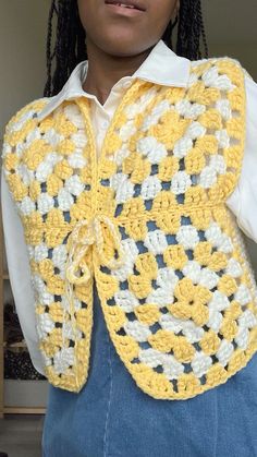 a woman wearing a yellow and white crochet vest with braids on it