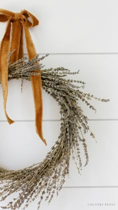 a dried lavender wreath on a white wooden wall with a brown ribbon tied around it