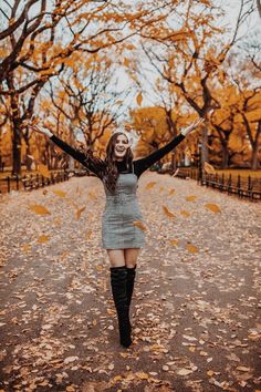 a woman standing in the middle of a leaf covered road with her arms outstretched up