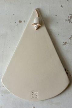 a white ceramic triangle with a bird on it's face hanging from the wall