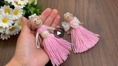 a hand holding two tiny pink tasselled angel ornaments with daisies in the background