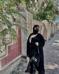 a woman in black is walking down the street with her hand on her face and holding a bag