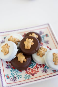 chocolate covered cookies with white frosting and teddy bear decorations on a decorative plate next to a cup of coffee