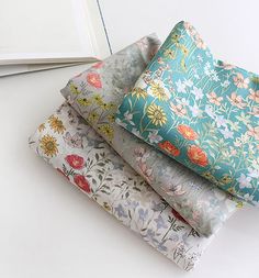 a stack of four different colored flowered sheets on top of each other next to an open book