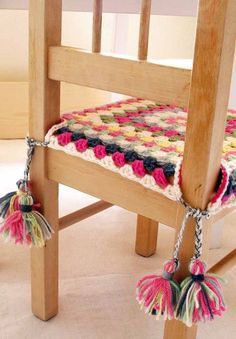 a crocheted seat pad with tassels attached to the back of a wooden chair