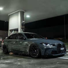 a grey car is parked in front of a gas station at night with its lights on