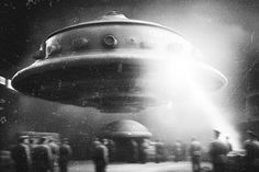 a black and white photo of people standing in front of a large object that looks like a flying saucer