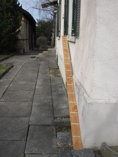 an empty sidewalk next to a white building with green shutters and windows on both sides