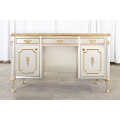 a white desk with gold trimmings and drawers on the top, in front of a curtained window