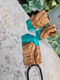 two wooden earrings with green ribbon attached to them on a stone surface next to plants