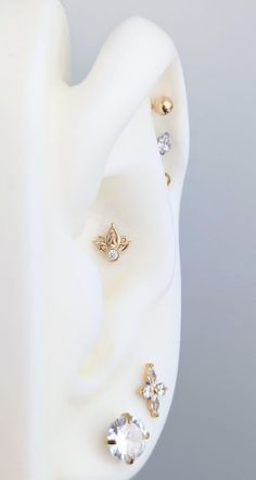 three pairs of ear piercings on top of a white plastic headpiece with gold and clear stones