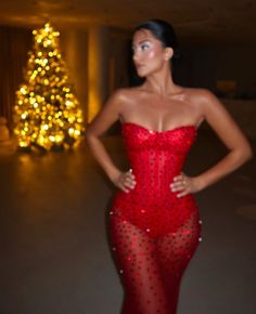 a woman in a red dress standing next to a christmas tree with lights on it