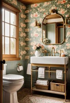 a bathroom with floral wallpaper and a gold sink, mirror, toilet, and window