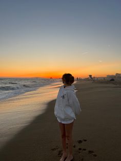 a woman standing on top of a sandy beach next to the ocean at sun set