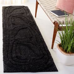 a black rug on the floor next to a chair and potted plant in a living room