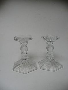 two clear glass candlesticks sitting side by side on a white surface with one candle in the middle