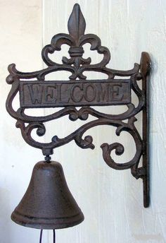 a metal bell with a welcome sign hanging from it's side next to a white wall