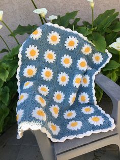 a crocheted blanket sitting on top of a wooden chair in front of flowers