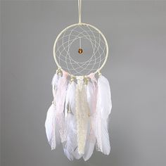 a white and pink dream catcher hanging from a hook on a gray wall with an orange bead in the center