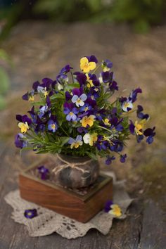 purple and yellow pansies in a vase on a wooden table with lace doily