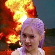 a woman with purple hair standing in front of a large explosion that has been set on fire