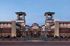 two tall buildings with clocks on each of them'sides, and people walking around