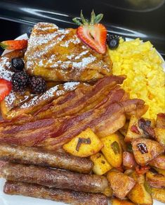 the breakfast plate is full of bacon, scrambled eggs, and other food items with strawberries on top