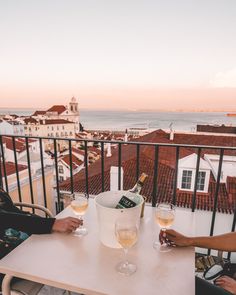 two people sitting at a table with glasses of wine on top of it, overlooking the ocean