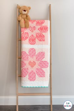 a teddy bear sitting on top of a pink and white quilt next to a ladder