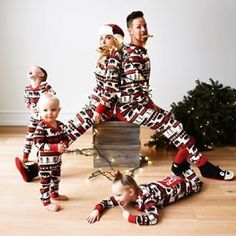 two adults and three children in matching christmas pajamas, standing on the floor next to a christmas tree