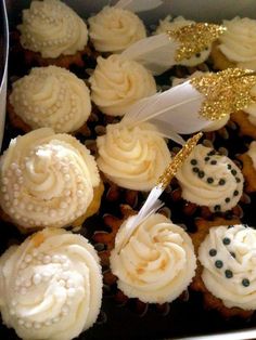 cupcakes with white frosting and gold decorations in a box on a table