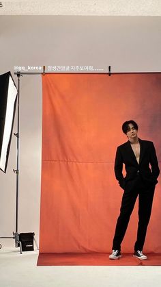 a man standing in front of a red backdrop wearing a black suit and white sneakers