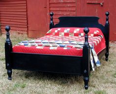 a bed sitting in the grass next to a red barn with a quilt on it