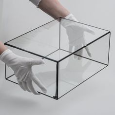 a person's hand in white gloves reaching into a glass box that is filled with something