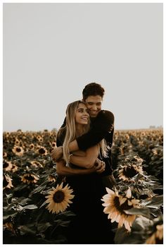 a man and woman hugging in the middle of a field of sunflowers at sunset