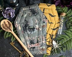 three napkins with cats and bats on them next to some green plants, candles and spoons