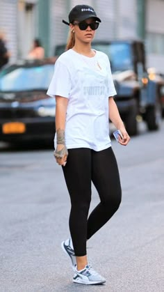 a woman walking down the street wearing black leggings and a white t - shirt