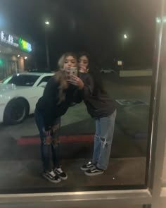 two women are taking a selfie in front of a store window with their cell phones