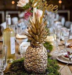 a pineapple centerpiece on top of a moss covered table with wine glasses and plates