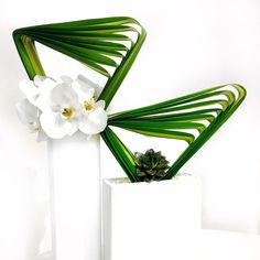 two white vases with flowers in them on a table next to a planter