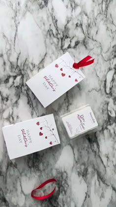 three white cards with red ribbon tied to them sitting on a marble counter top next to each other