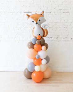 a balloon tower with balloons and a fox head on top, in front of a white brick wall