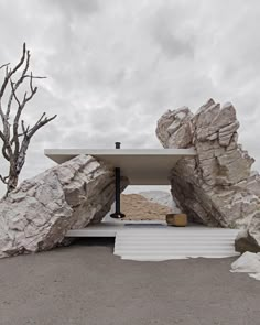 an outdoor table surrounded by large rocks on the beach with a tree in the background