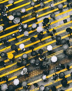 an overhead view of people with umbrellas crossing the street in front of yellow lines