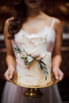 a woman holding a wedding cake with flowers on it