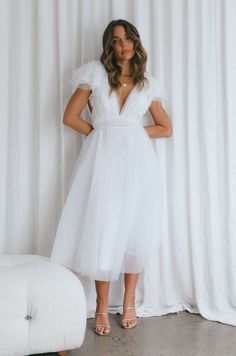 a woman standing in front of a white curtain wearing a dress with short sleeves and high heels