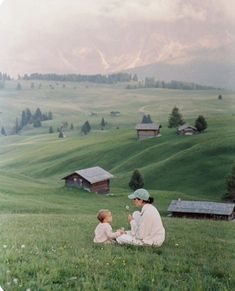 an old photo of two people sitting on the grass in front of a small village