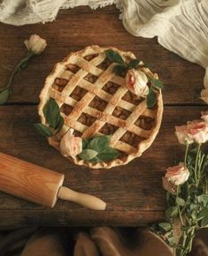 a pie sitting on top of a wooden table next to flowers and a rolling pin